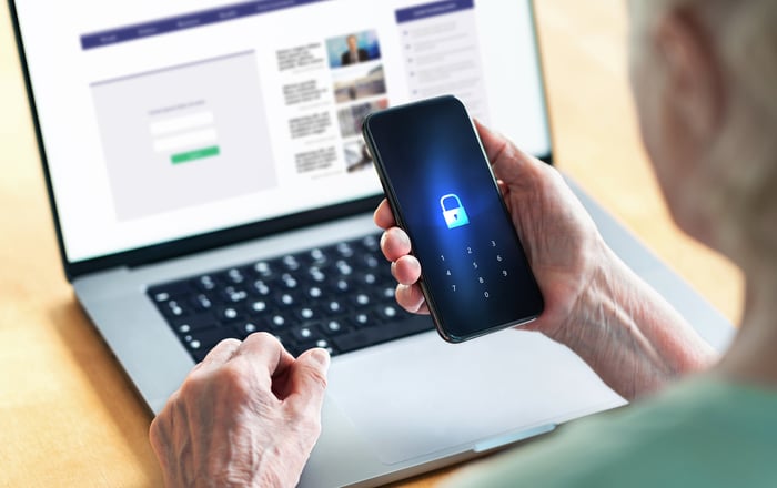 Person holding a locked smartphone while doing a search on their laptop. 