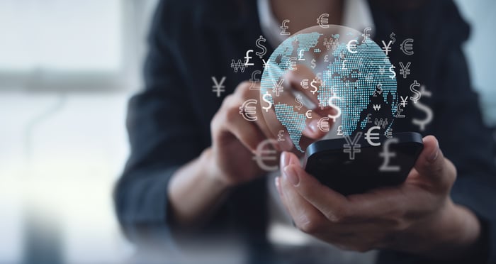 Hand holding a smartphone with digital currency symbols floating around it. 