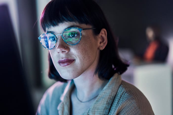 A person looking at a screen and you can see data reflected in their glasses. 