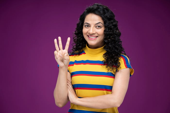 Someone holding up three fingers and smiling.