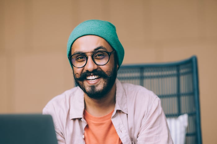 Someone with glasses is seated and smiling.