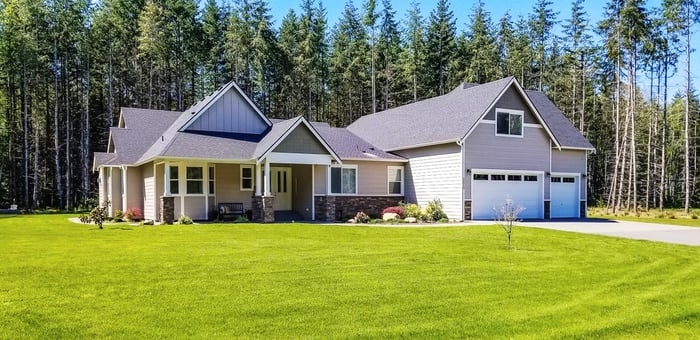 Home sitting on a large lot, with mature trees in the background.