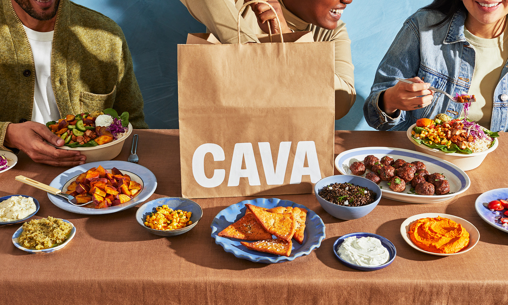 CAVA stock - people eating on a table wit CAVA logo in view_CAVA
