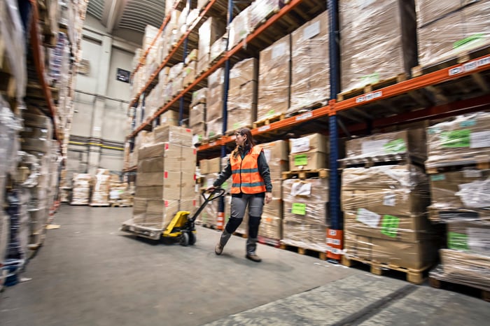 A warehouse worker pulls a pallet machine.