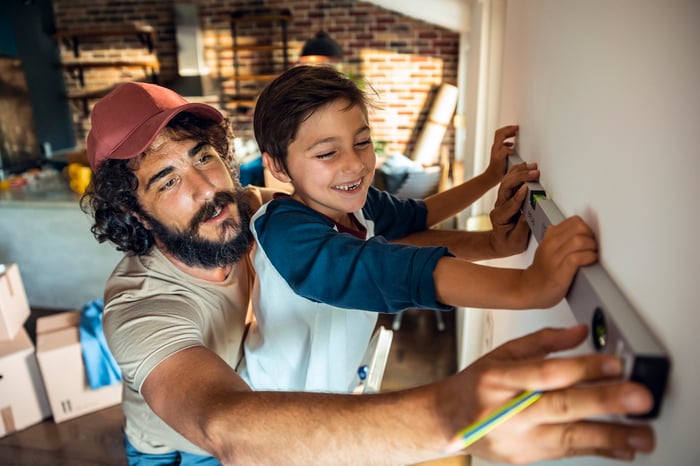A parent and child measure the wall while working on a home.