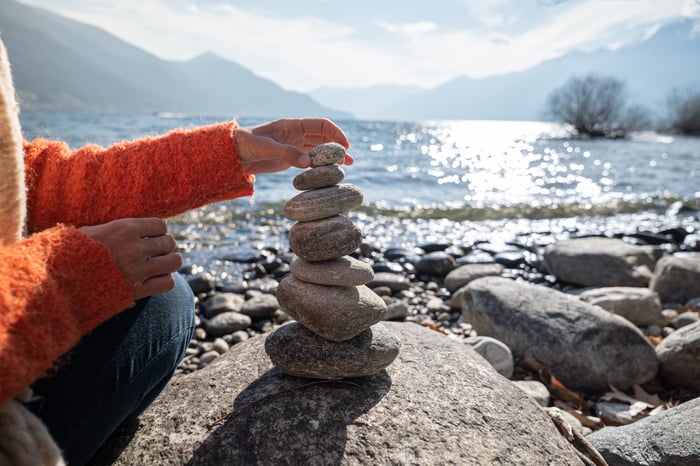 A person sitting on a rocky coast making a tower of rocks. 