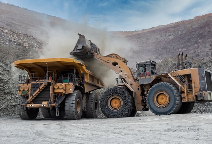 A heavy-duty loader is filling up a dump truck at a mine.