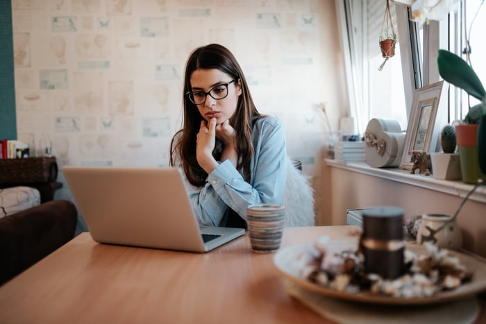 A person looking at their laptop screen, hands on their chin. 