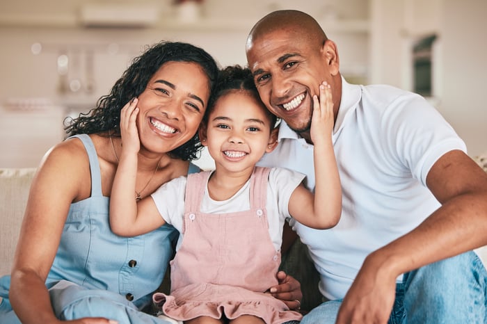 Three people together smiling while the middle one has hands on the others' faces.