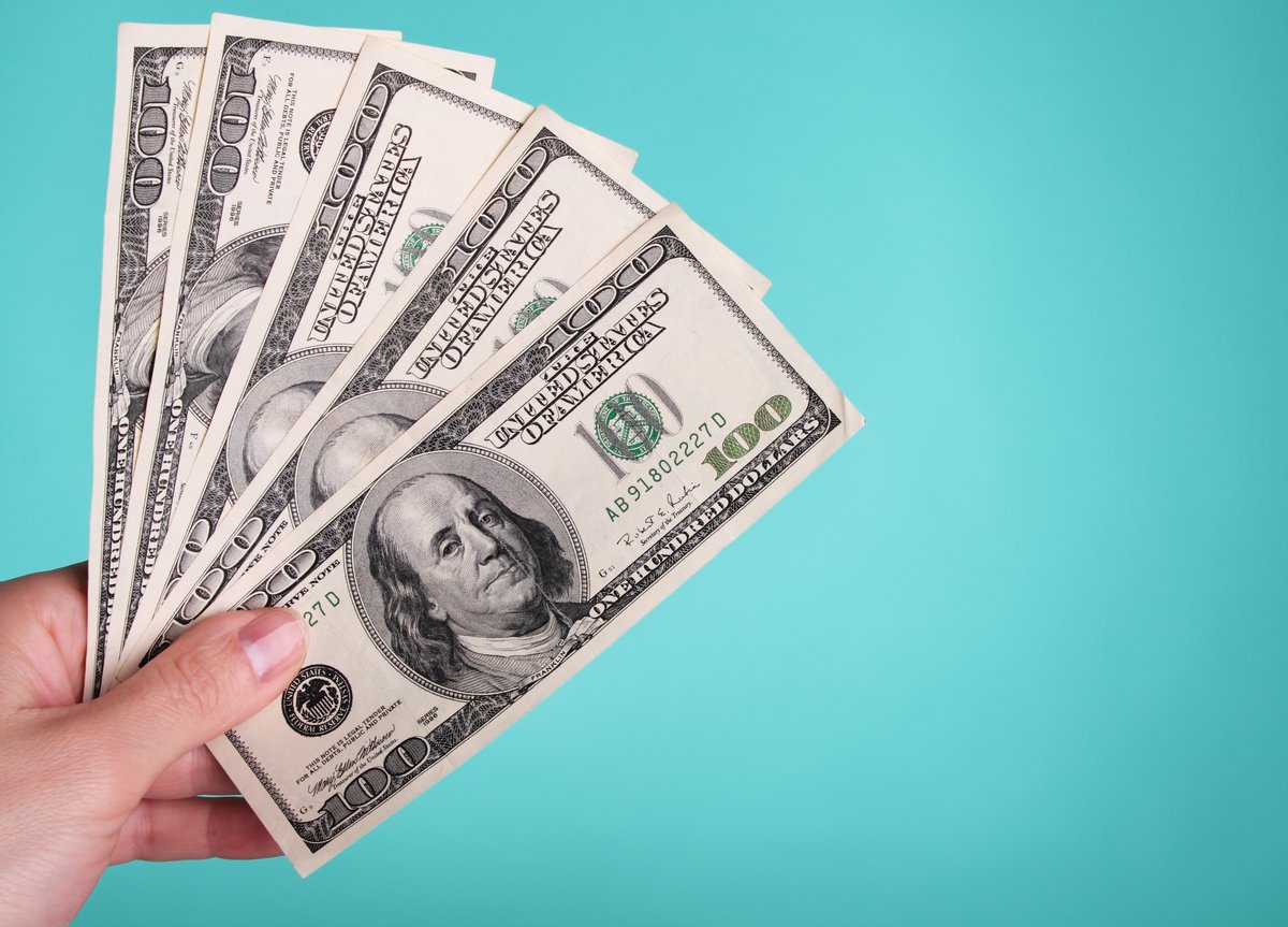 A person's left hand holding 5 $100 bills