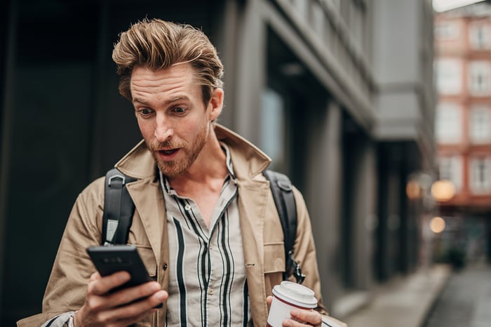 Surprised investor looking at smartphone on urban street.
