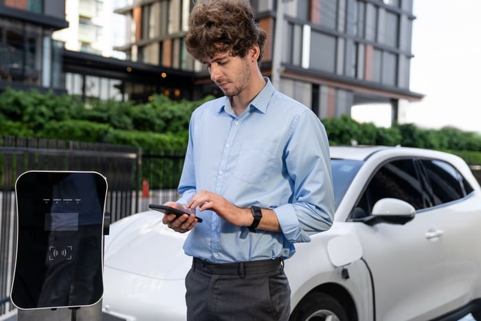 A person taps their smartphone while charging their car.