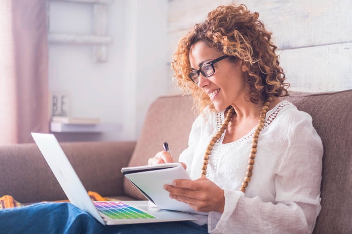 Person at home reviewing financial statements on a laptop while writing on a notepad.