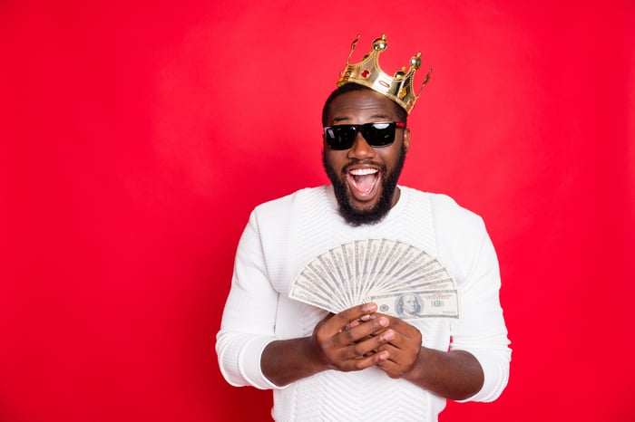 A man in a crown fans out a handful of cash.