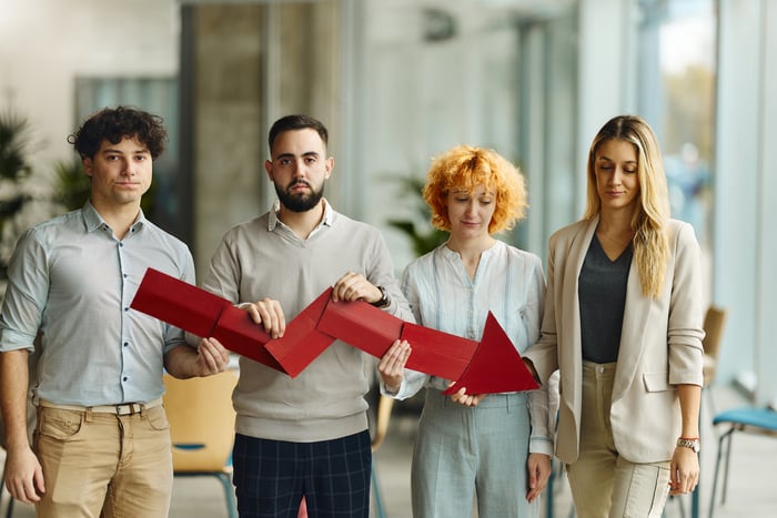 Four people stand in a row while holding a downward trending arrow. 