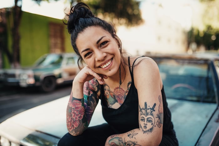 A young adult sitting on the hood of a car, smiling. 