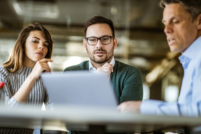 Three investors gather around a laptop as one explains the data shown on the screen to the others.