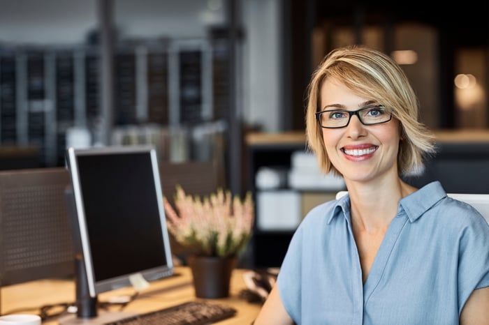 A smiling person next to a desk.