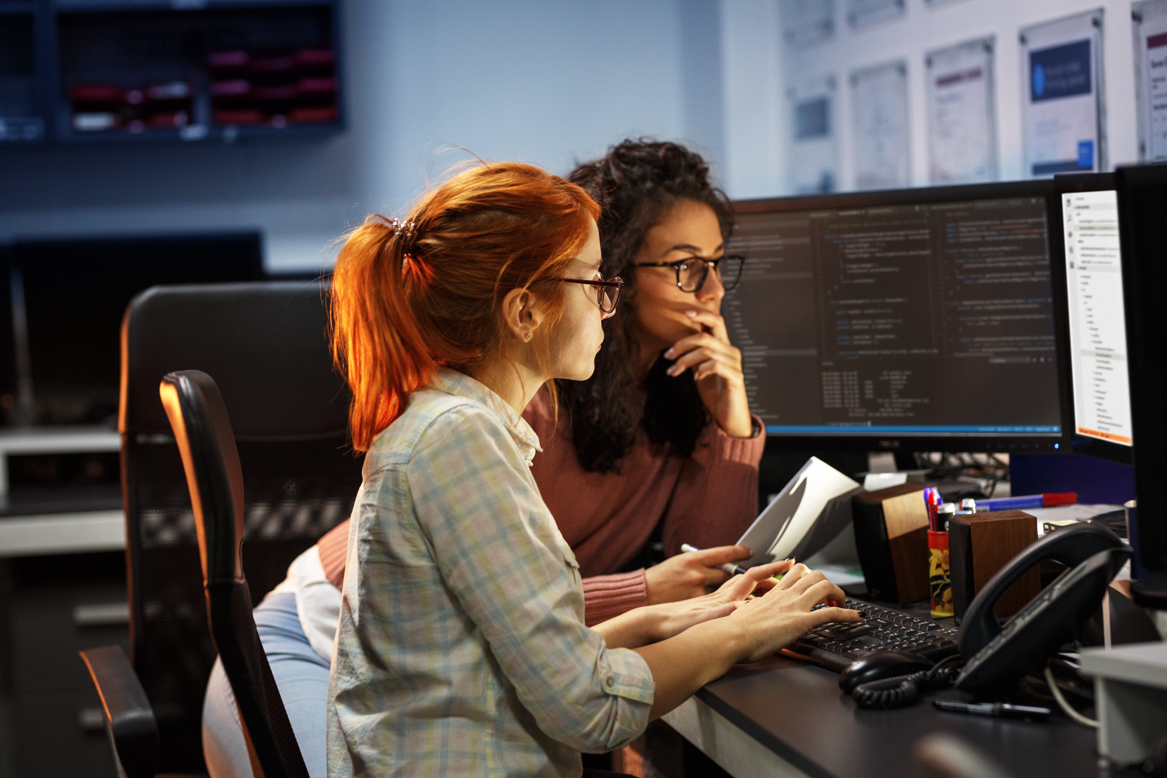 Two computer programmers working together while looking at computer screens
