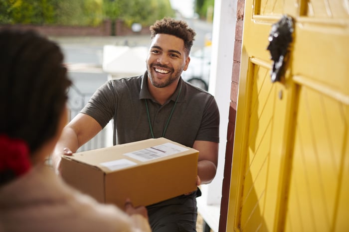 A smiling person delivering a package to a homeowner standing by the open front door. 