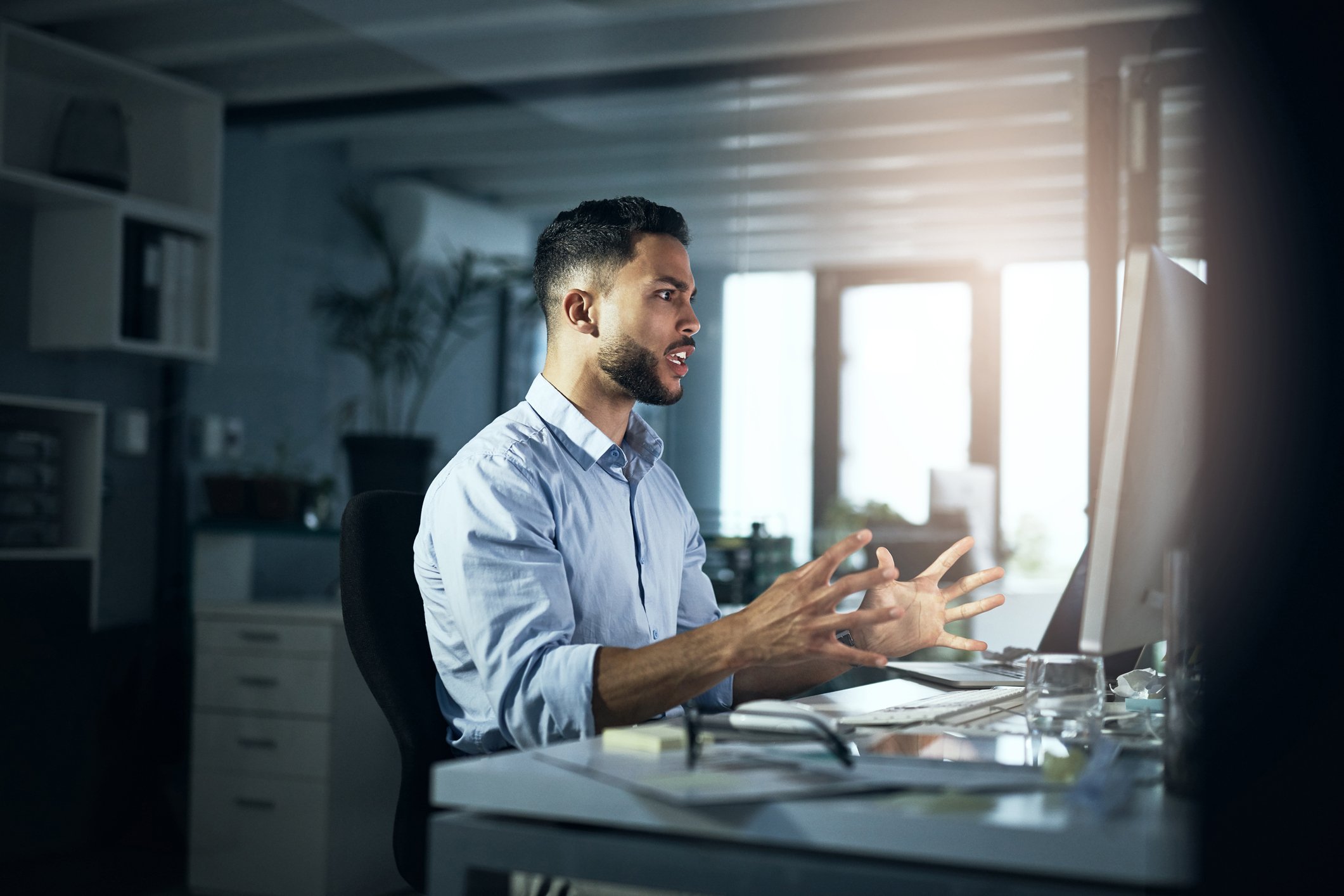 An angry person with hands outstretched looking at a computer monitor