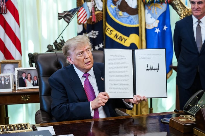 President Trump in the Oval Office holding up an executive order.