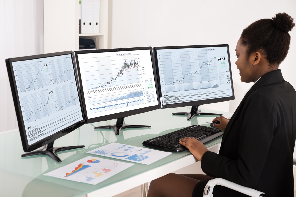 Analyst_analyzing_stock_charts_on_three_desktop_screens