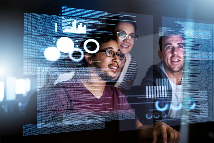 Software engineers look at a screen in holographic form. 