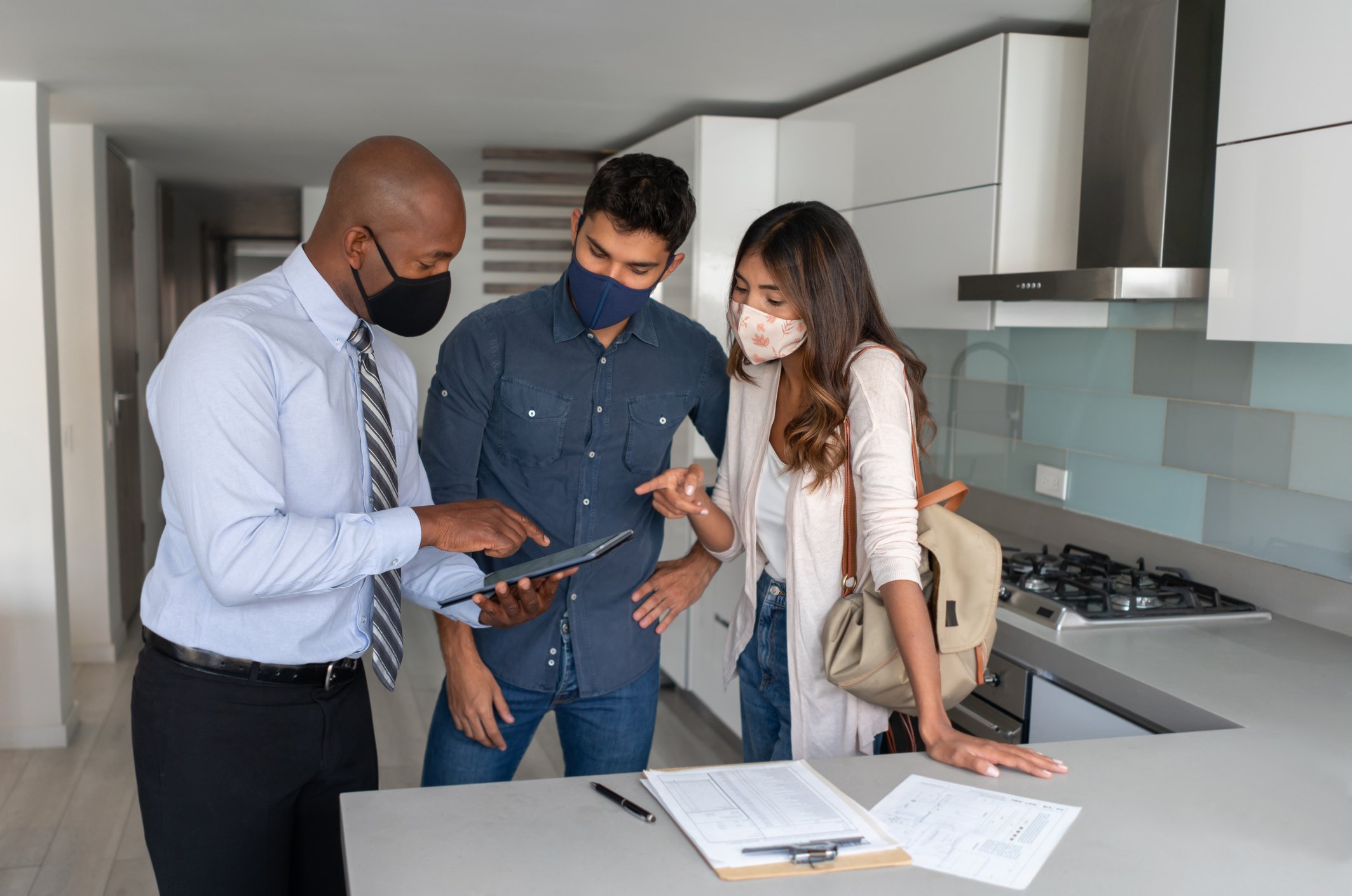 Two people conferring with another person in the kitchen of a home
