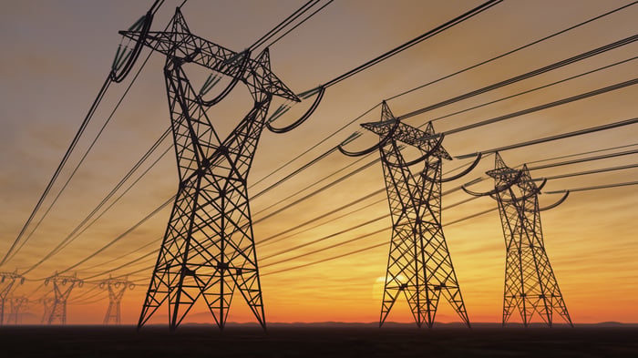 Overhead power lines and pylons against the backdrop of a setting sun.