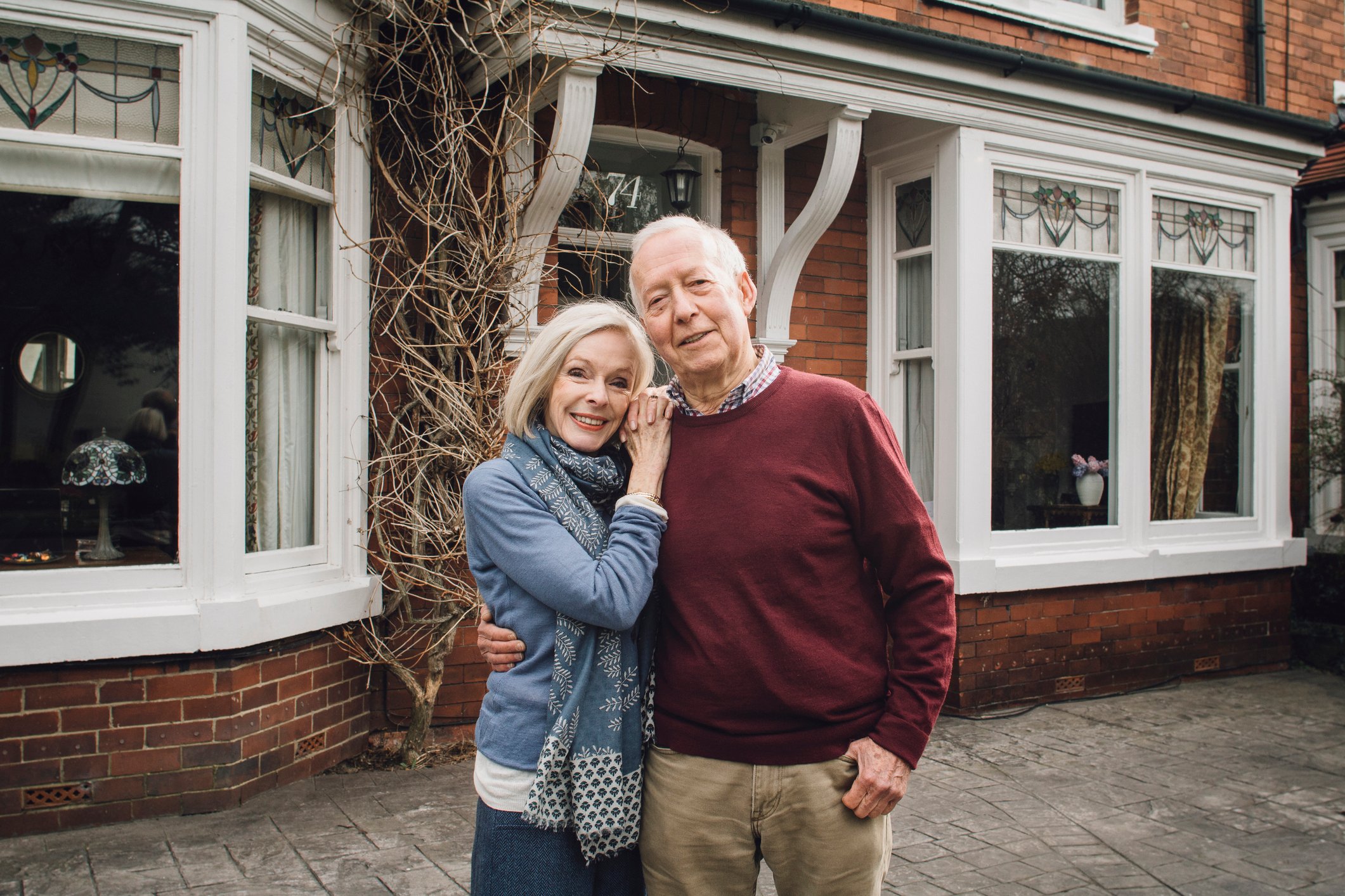 senior man and woman smiling and holding each other in front of a house -- home couple 30 year mortgage