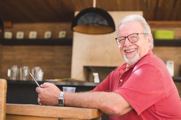 Person smiling while holding a smartphone at a table. 