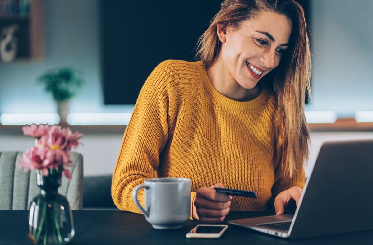 A person smiles while holding a credit card and sitting in front of a laptop computer.