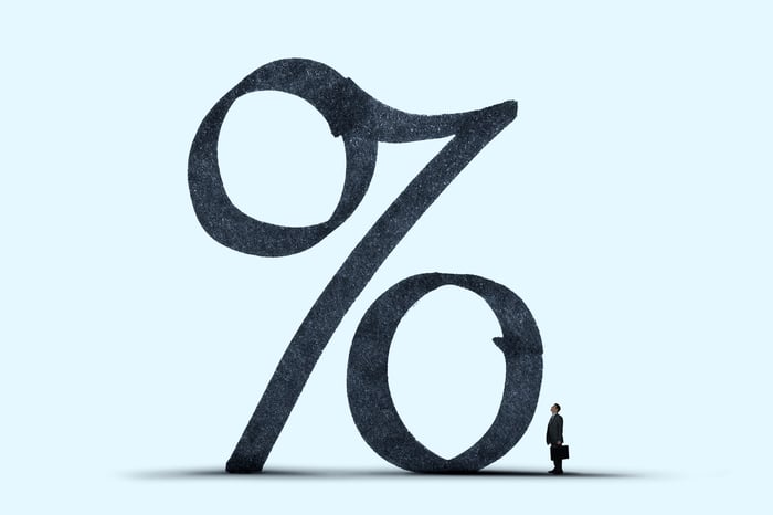An illustration of a percentage sign is shown with a silhouette of a small man carrying a briefcase standing next to it