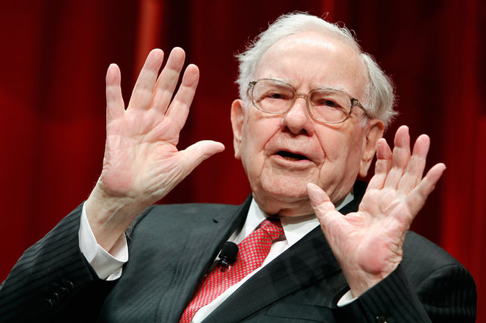 Legendary investor Warren Buffett in a dark gray suit and red tie.