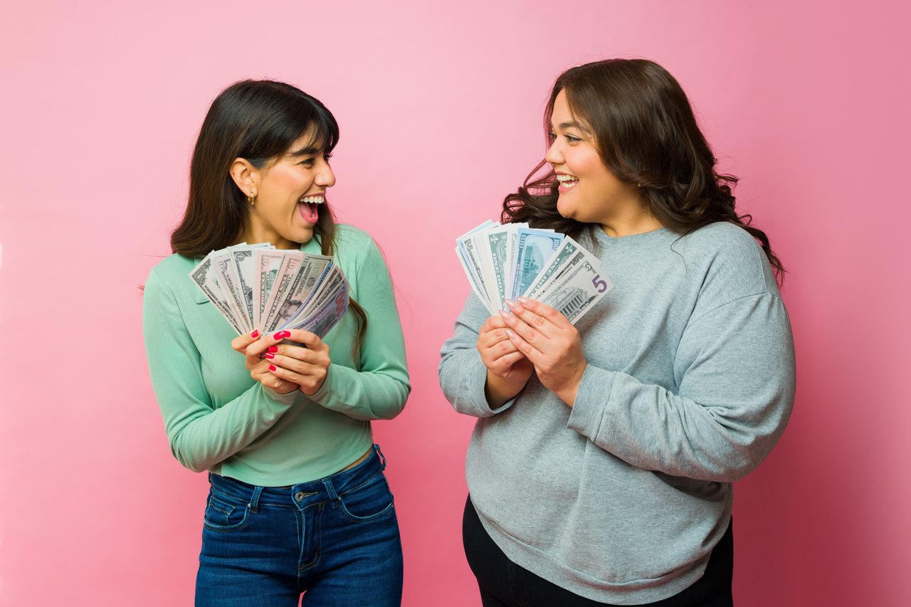 two smiling investors hold fanned out cash.