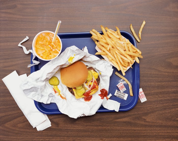 A fast food meal on a blue tray consisting of a cheeseburger, fries, and a soda.