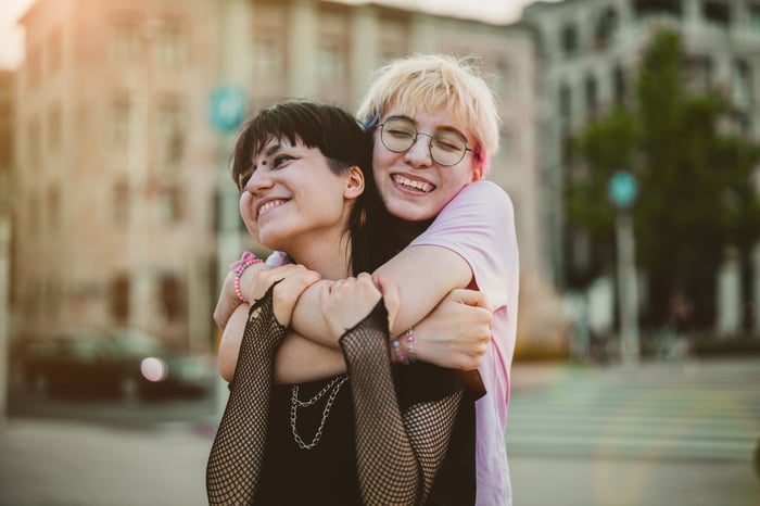 Two people smiling and hugging outdoors.