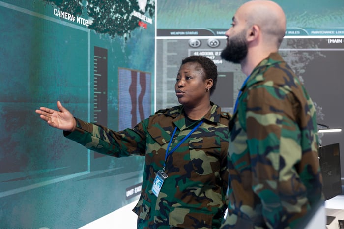 Two military personnel review data on a large command-center screen.
