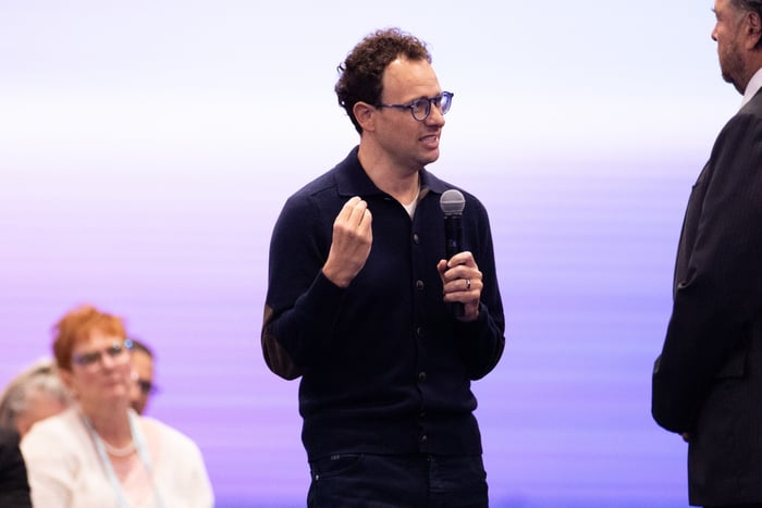 CEO Dario Amodei speaks into a microphone while gesturing during a discussion at an event.