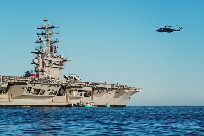 A U.S. Navy aircraft carrier in the ocean with a helicopter flying overhead.