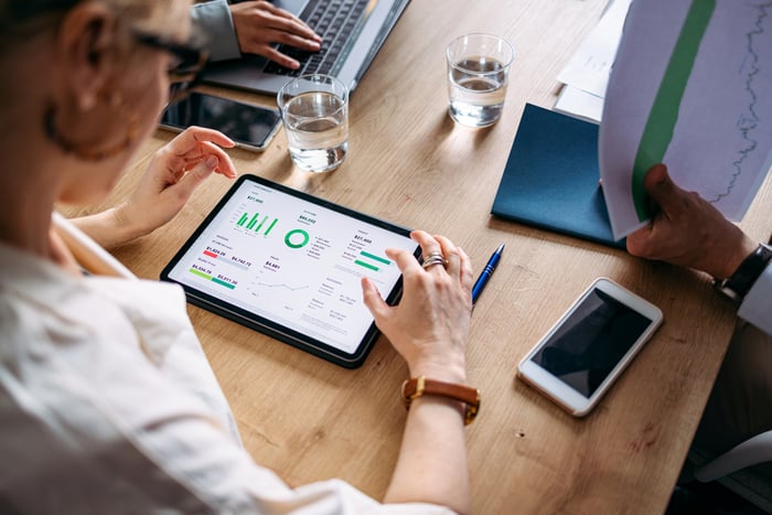 An investor reads a tablet screen with stock market details and charts.