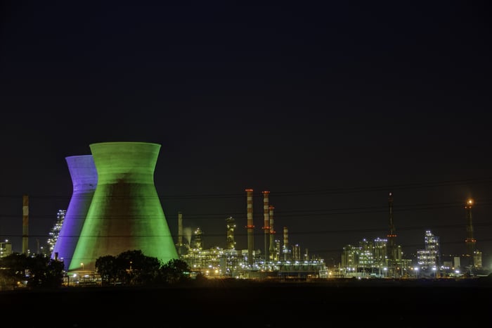 An energy plant, with two floodlit hyperbolic cooling towers in front of smokestacks, distillation columns, and a flare stack.