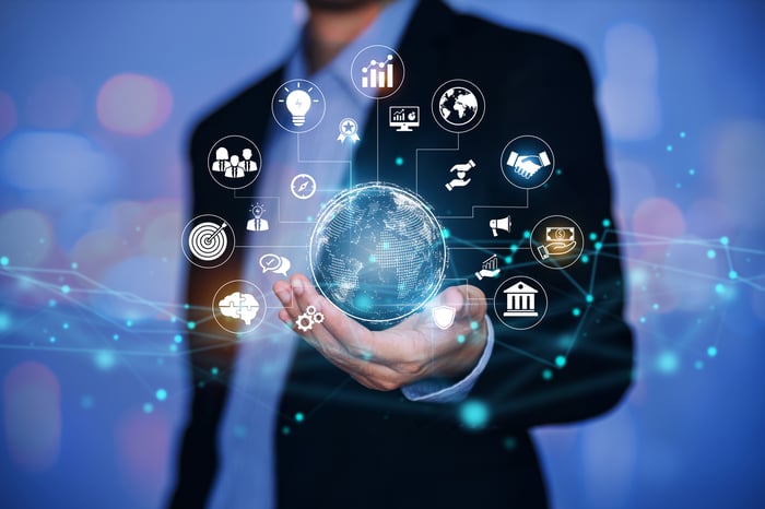 An investor holds a digital image of a globe, orbited by symbols of international business.
