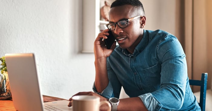 A man on a phone call while sitting in front of his laptop.