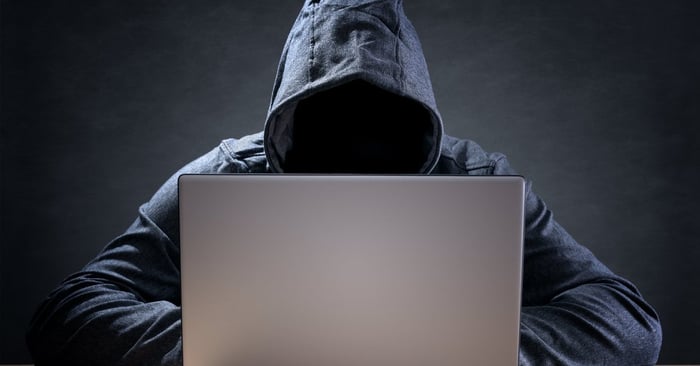 A cyber criminal wearing a hoodie and using a laptop.