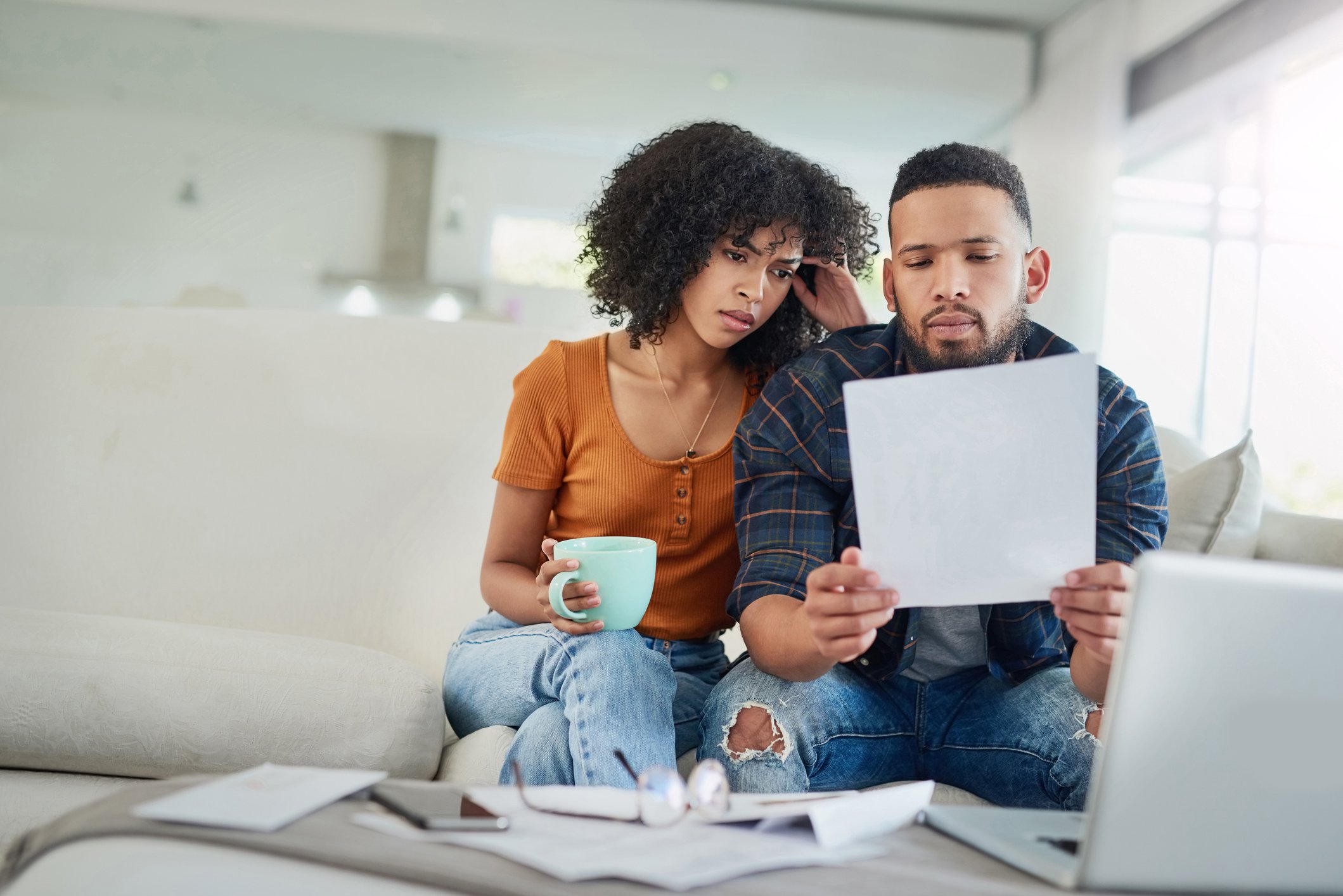 Worried couple sitting on couch while looking at document