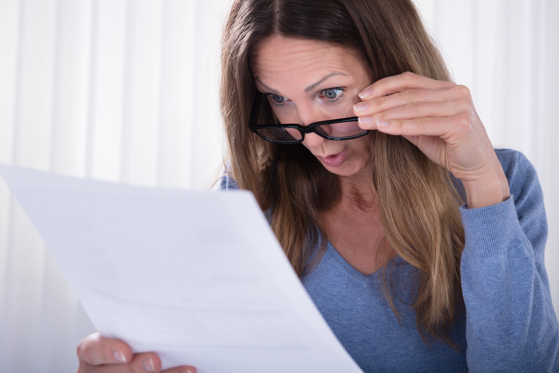 Woman holding down her glasses to examine a document more closely.