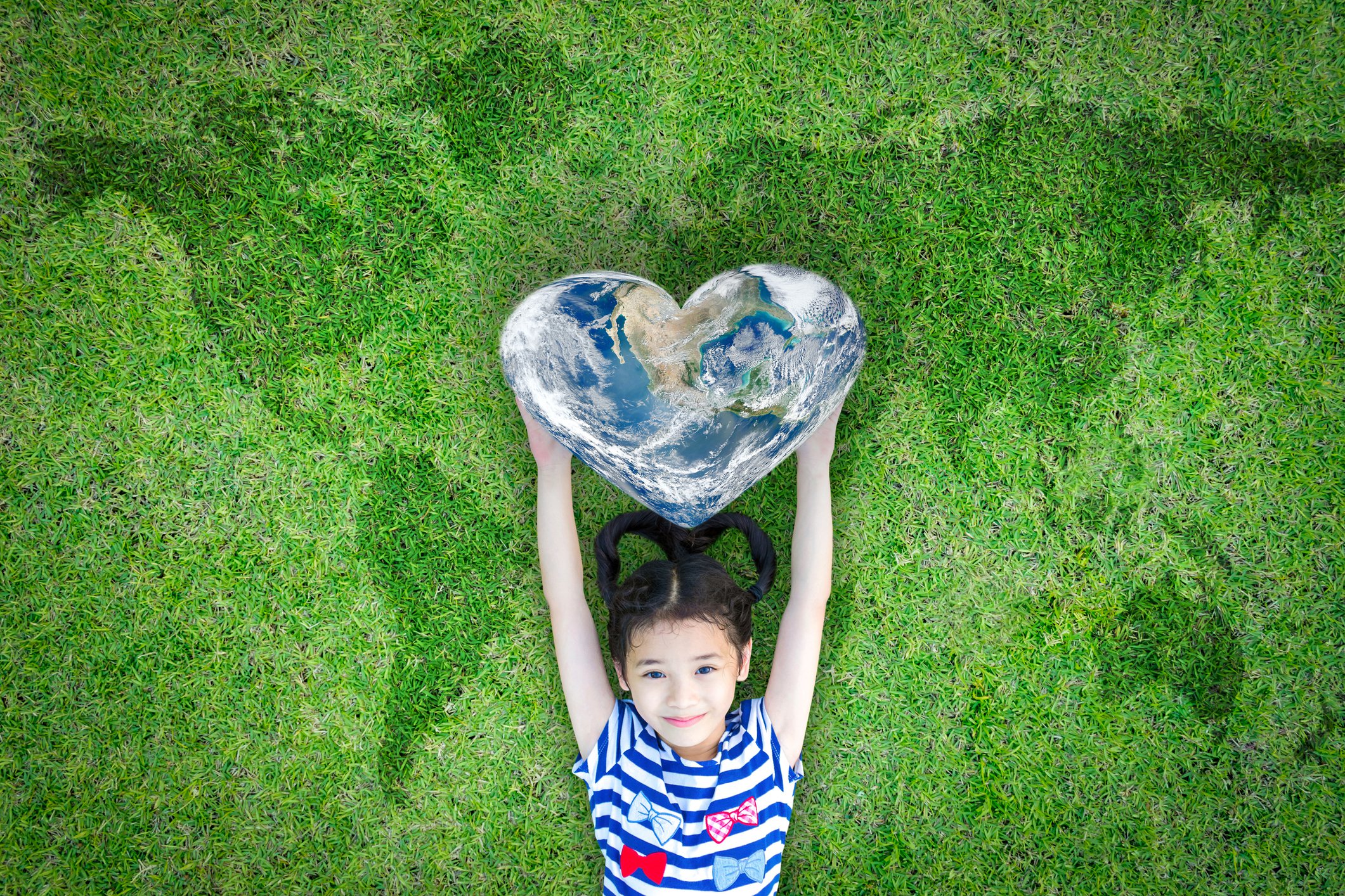 Girl holding heart shaped world while laying on grass with a map of the world