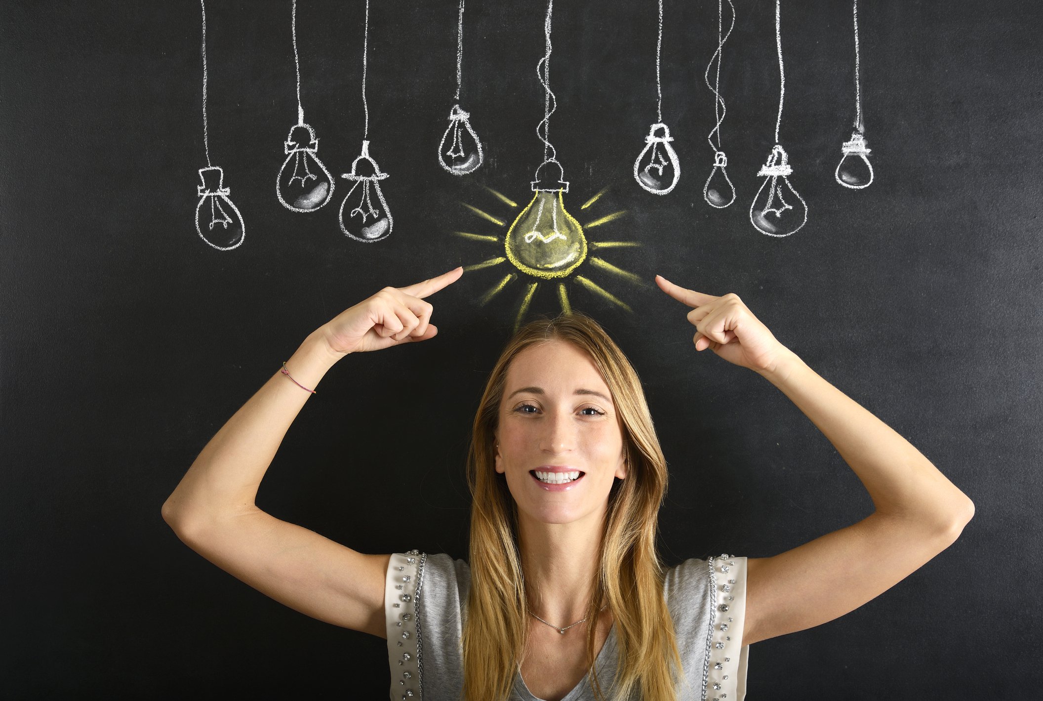 a woman pointing to a lit chalk lightbulb above her head